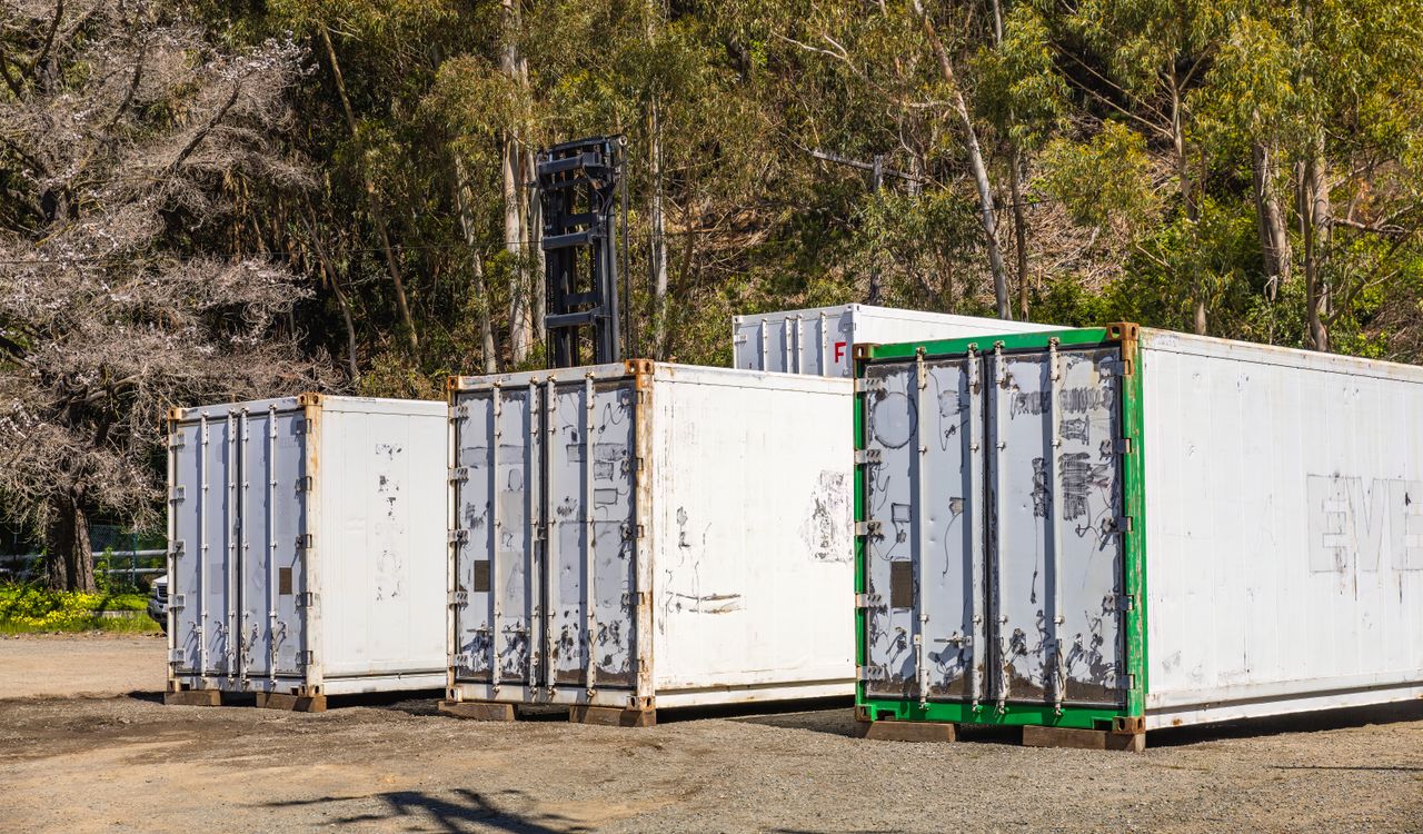 Beranda Group of white shipping containers set against a forest backdrop, illustrating transportation logistics.