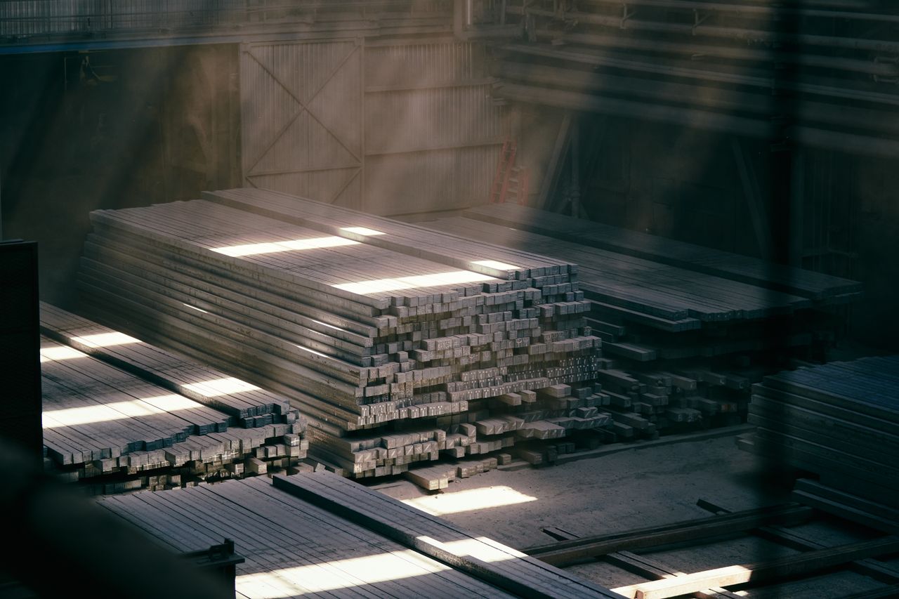 Beranda Sunlight streaming through an industrial warehouse highlighting stacked metal beams.