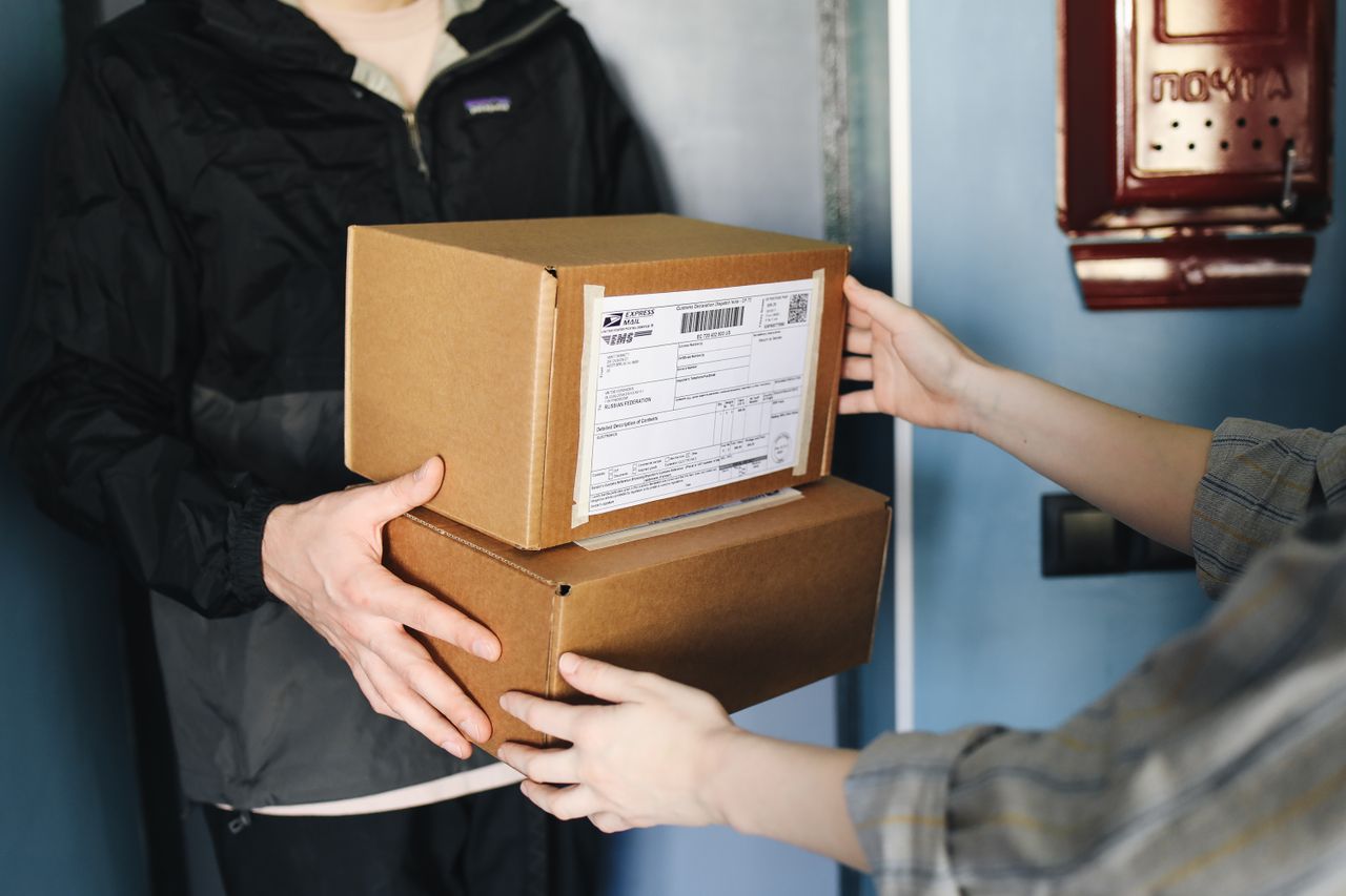 Beranda Close-up of hands exchanging cardboard boxes indoors, symbolizing delivery service.